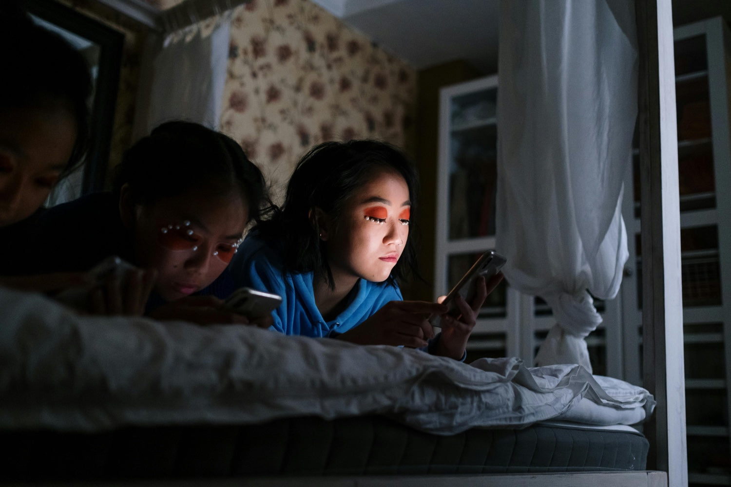 Three girls holding their phones while in bed