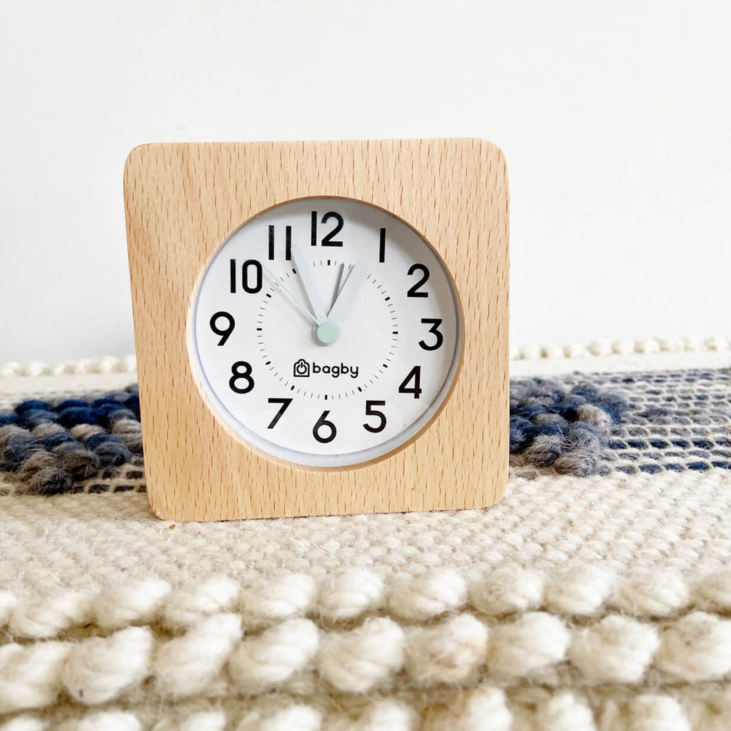 Square clock with wooden frame and white face on textured white and dark blue surface