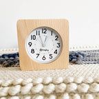 Square clock with wooden frame and white face on textured white and dark blue surface