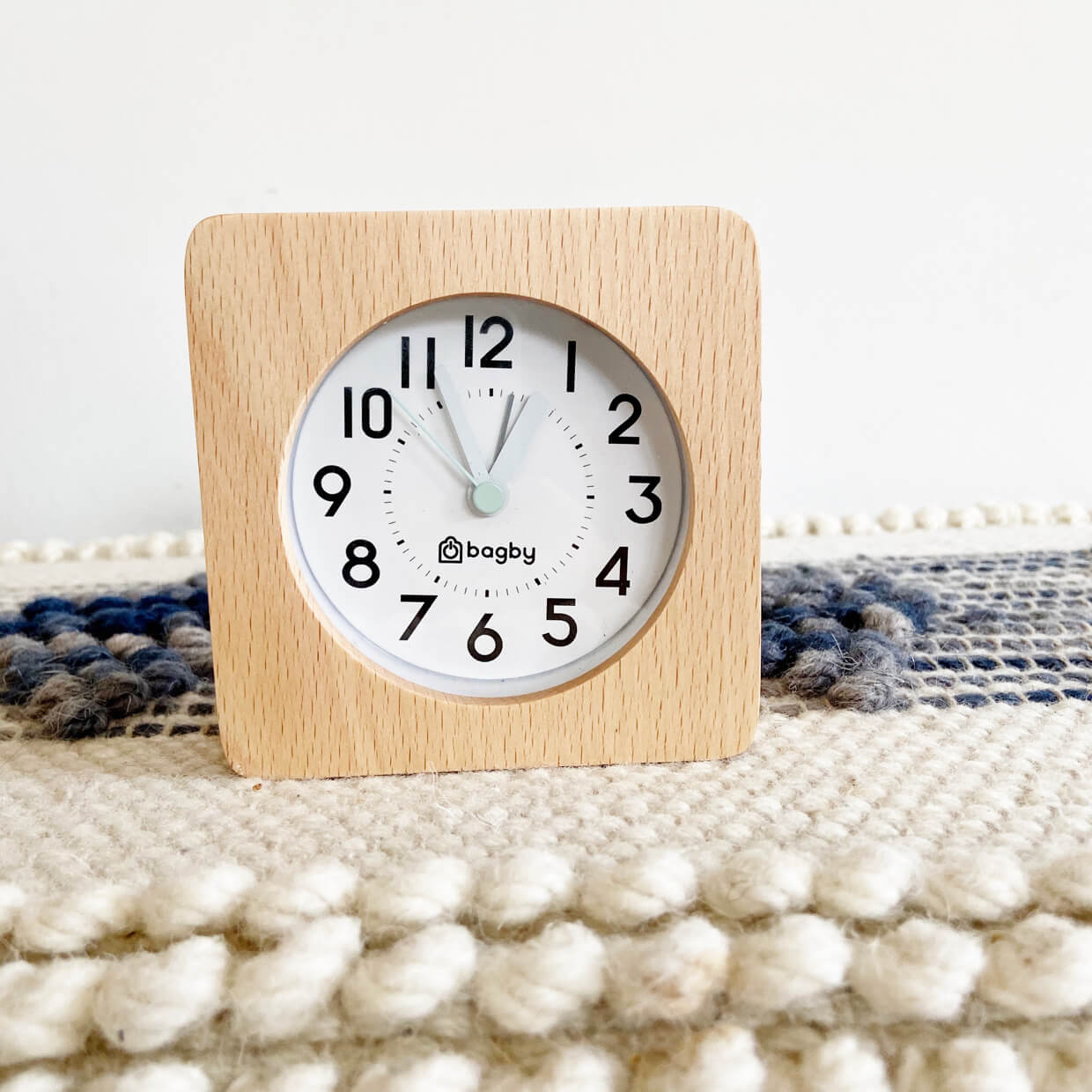 Square clock with wooden frame and white face on textured white and dark blue surface