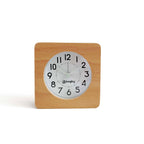 Square clock with wooden frame and white face on plain white surface indoors