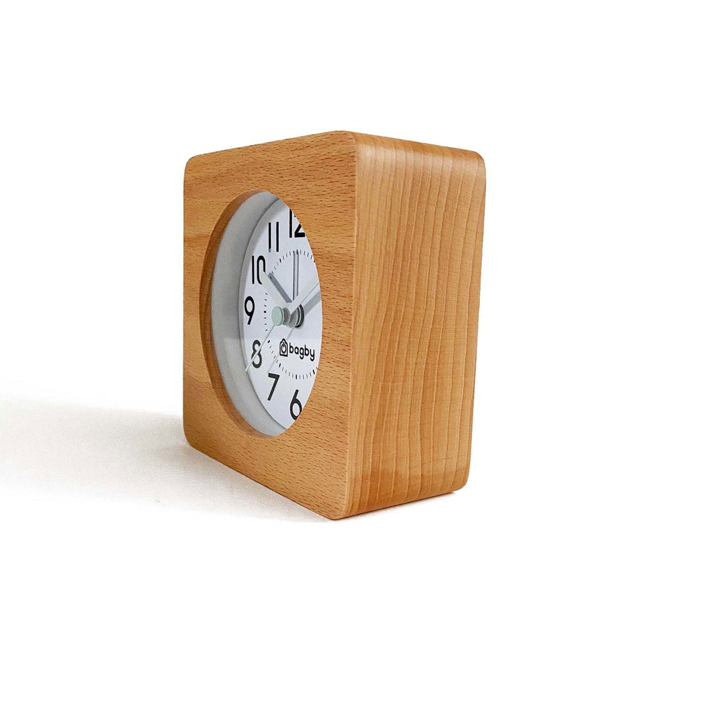 Small square clock with light brown wooden texture and white face on white surface indoors