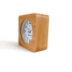 Small square clock with light brown wooden texture and white face on white surface indoors