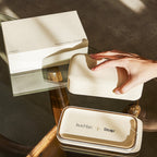 Hand lifting lid of beige box on glass table with white box in background
