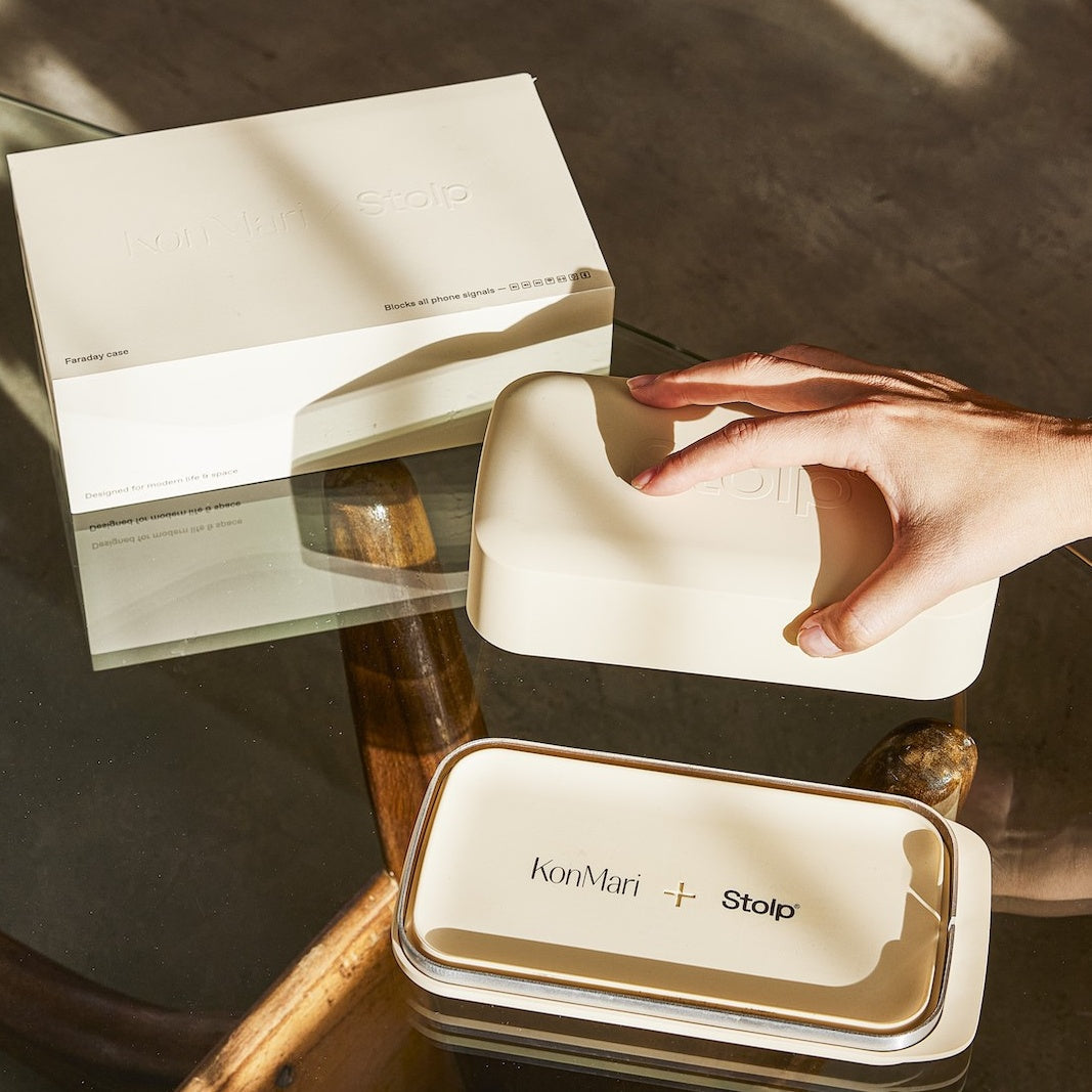 Hand lifting lid of beige box on glass table with white box in background