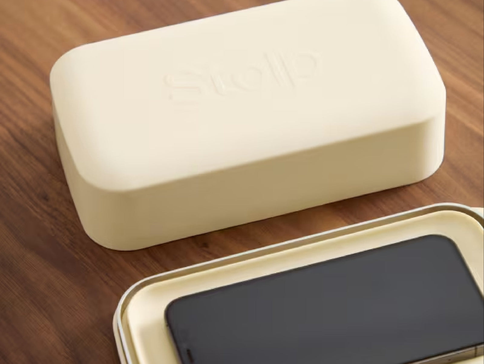 The closed Stolp Faraday phone box on a walnut table, its lid debossed with the Stolp mark, beside an open tray holding a phone