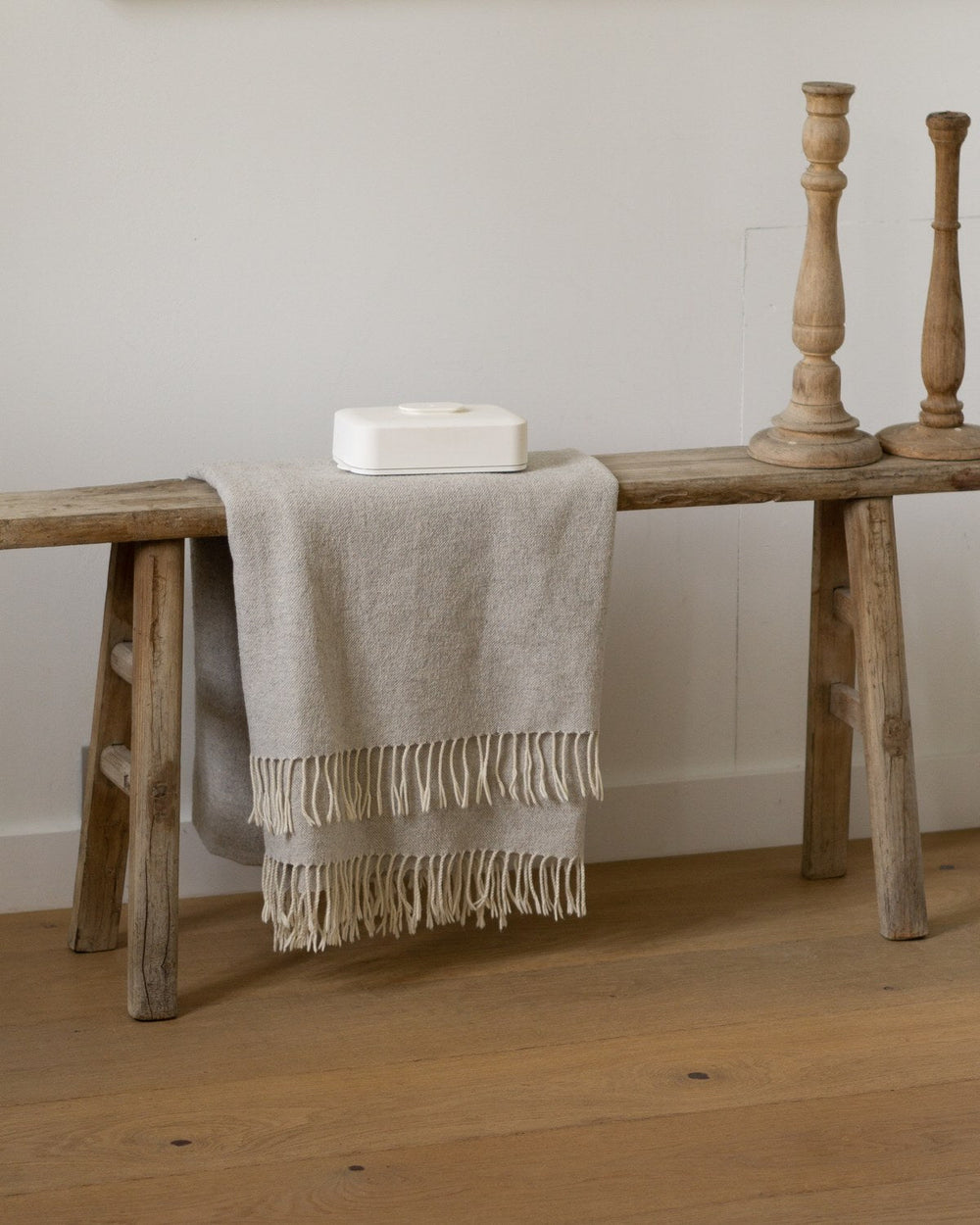 A closed sand Stolp Faraday phone box at rest on a weathered wood bench, beside two wooden candlesticks and a fringed linen throw.